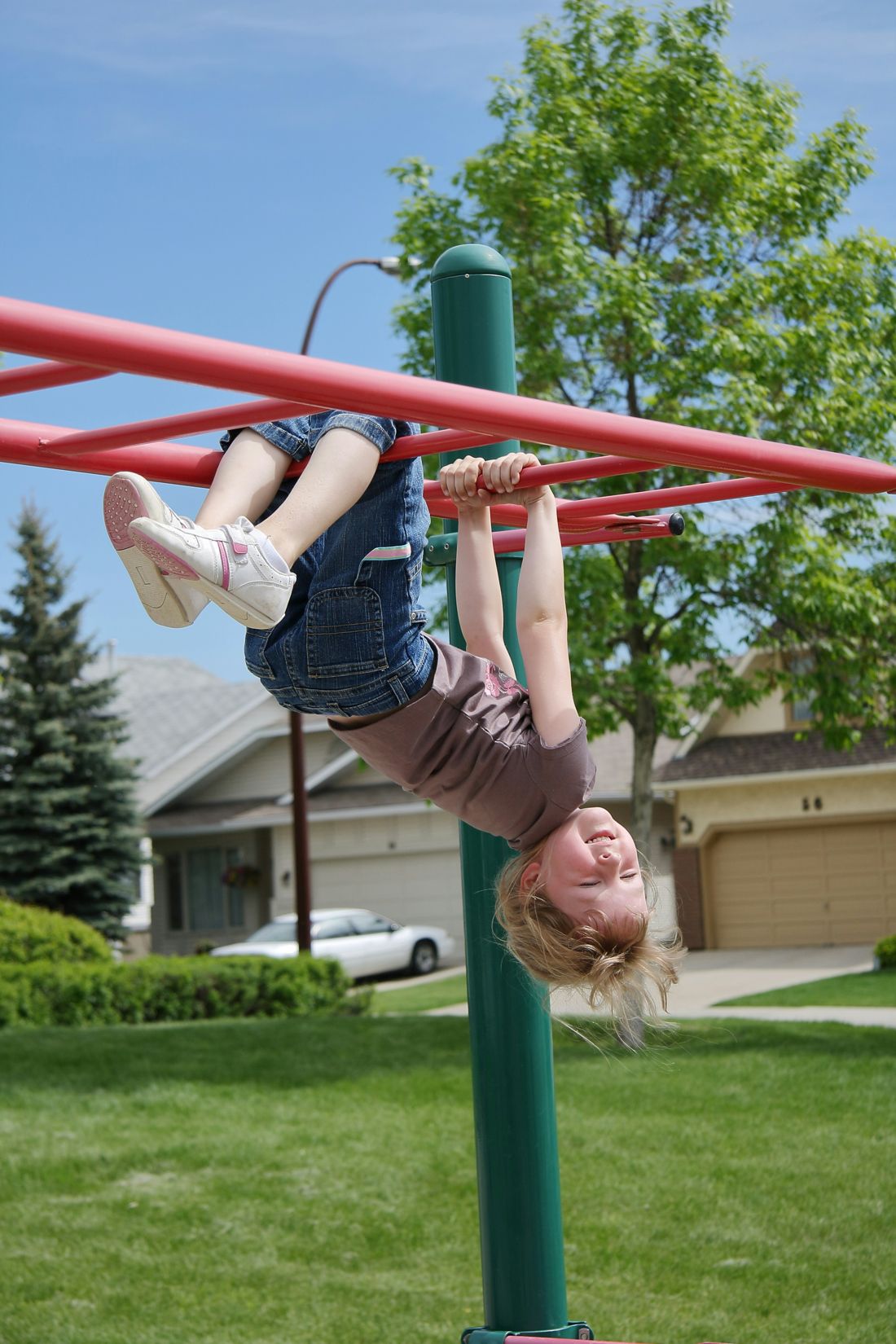 A girl hanging upside down from playground bars, smiling